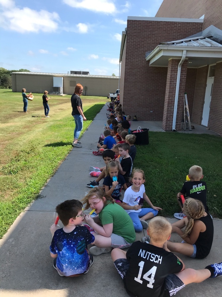 students sitting on sidewalk outside of school with teacher - fun friday